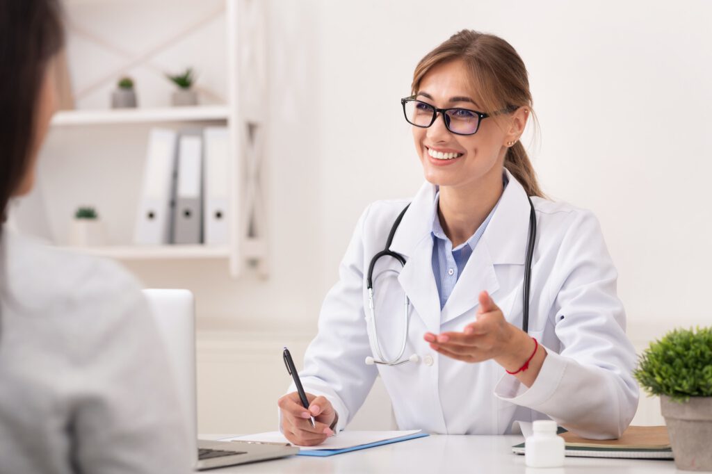 Smiling Doctor Woman Talking With Unrecognizable Patient Sitting In Office